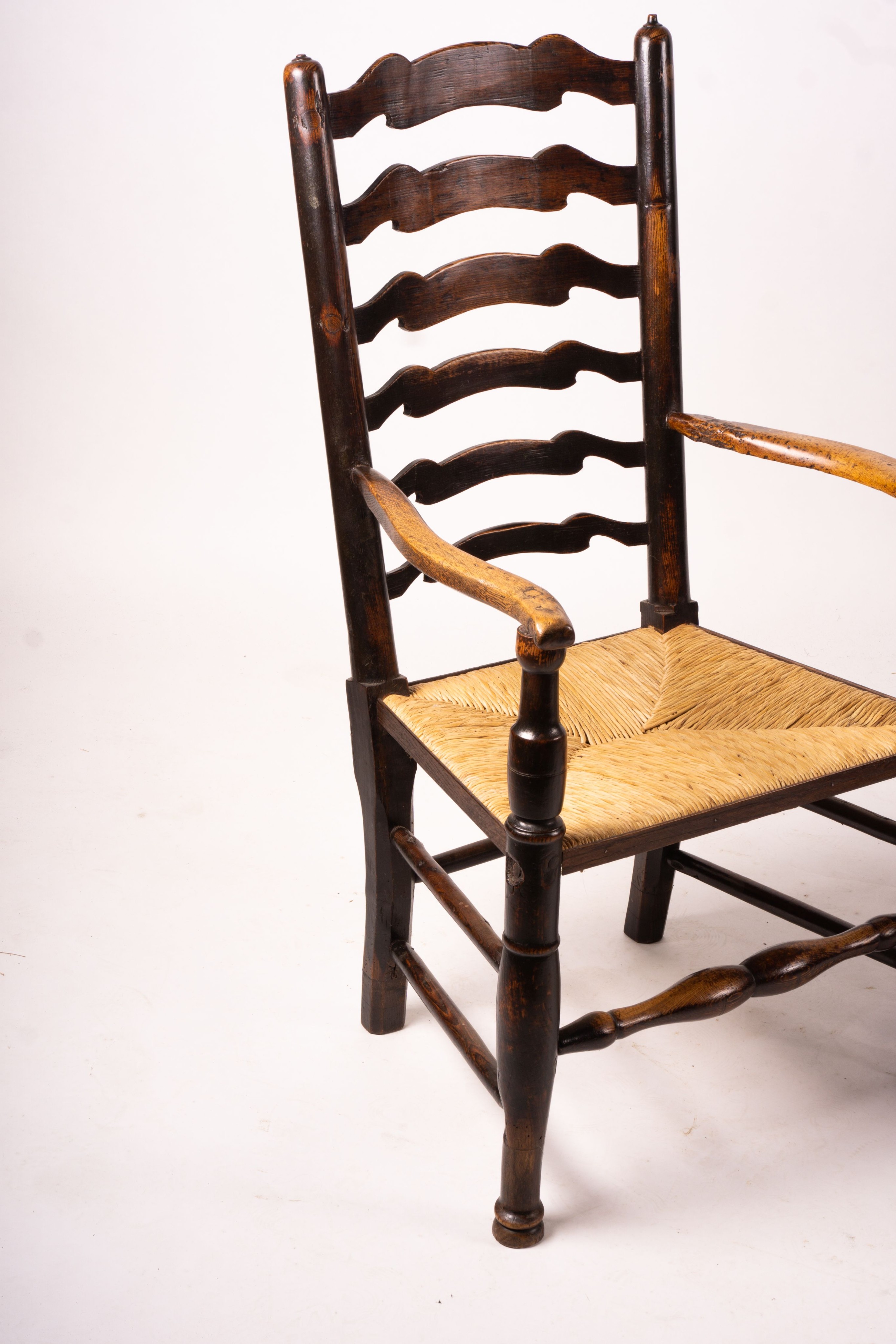 A pair of early 19th century Lancashire ash and fruitwood rush seat ladderback elbow chairs, width 60cm, depth 46cm, height 110cm